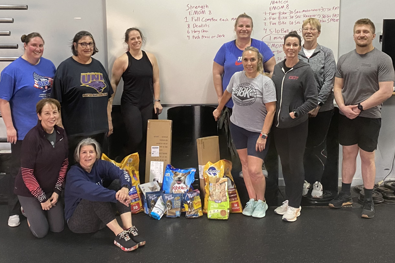 Large group of smiling people in a gym with pet food donations in center.