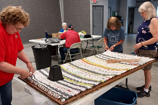 photo of People weaving plastic bags into table-sized mats.